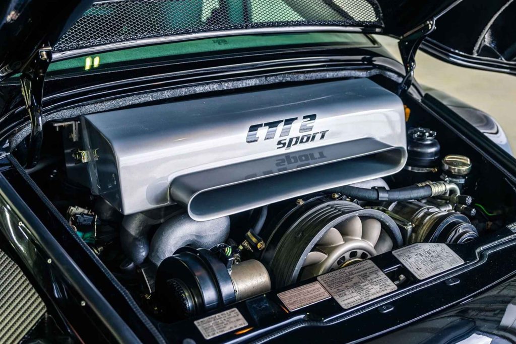 Engine bay of the Ruf CTR2 Sport with the rear lid open, showing the silver engine cover bearing the "CTR2 Sport" lettering, large turbocharger, cooling fan, and ancillary components of the flat-six engine.