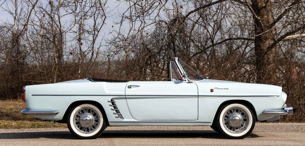 Pure side profile of the pale blue Renault Floride cabriolet with roof down, highlighting the elegant long bonnet, chrome side trim, louvred rear quarter vents, and wire wheels with whitewall tyres.
