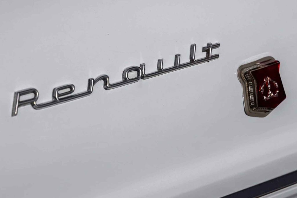 Close-up of the chrome italic "Renault" script badge and small red shield emblem on white bodywork.
