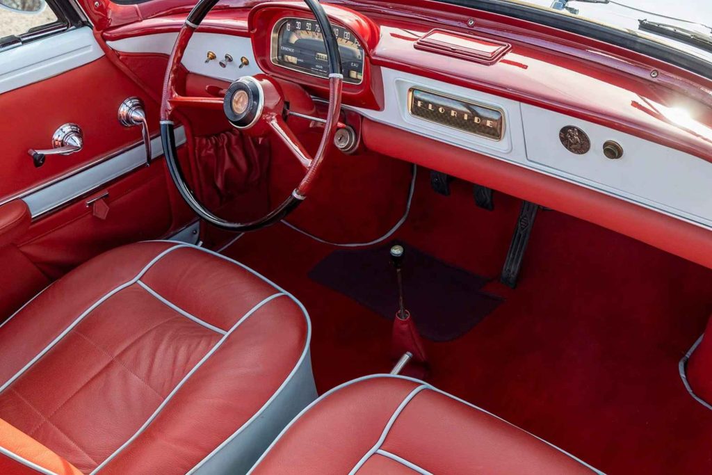 Passenger-side interior view of a red Renault Floride showing the matching red leather bucket seats with white piping, centre-mounted gear lever, red carpeting, and "Floride" dashboard badge.