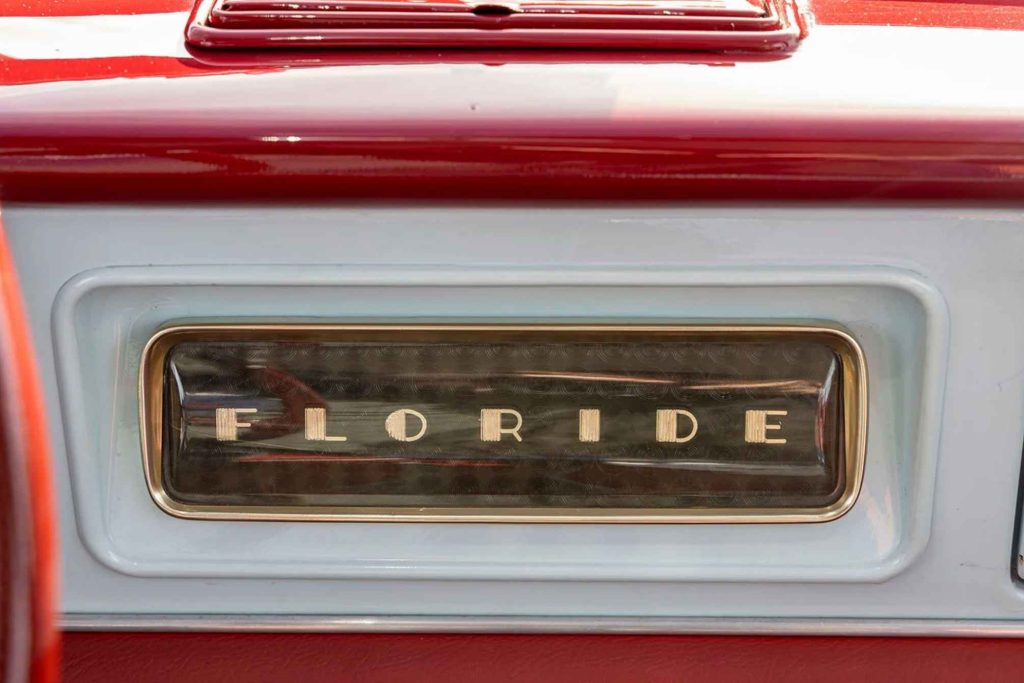 Close-up of the "Floride" name badge on the dashboard, set in a chrome-edged rectangular panel against a grey background with red bodywork above.