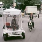 BBC archival footage showing a white cylindrical electric microcar known as Witkar navigating a city intersection