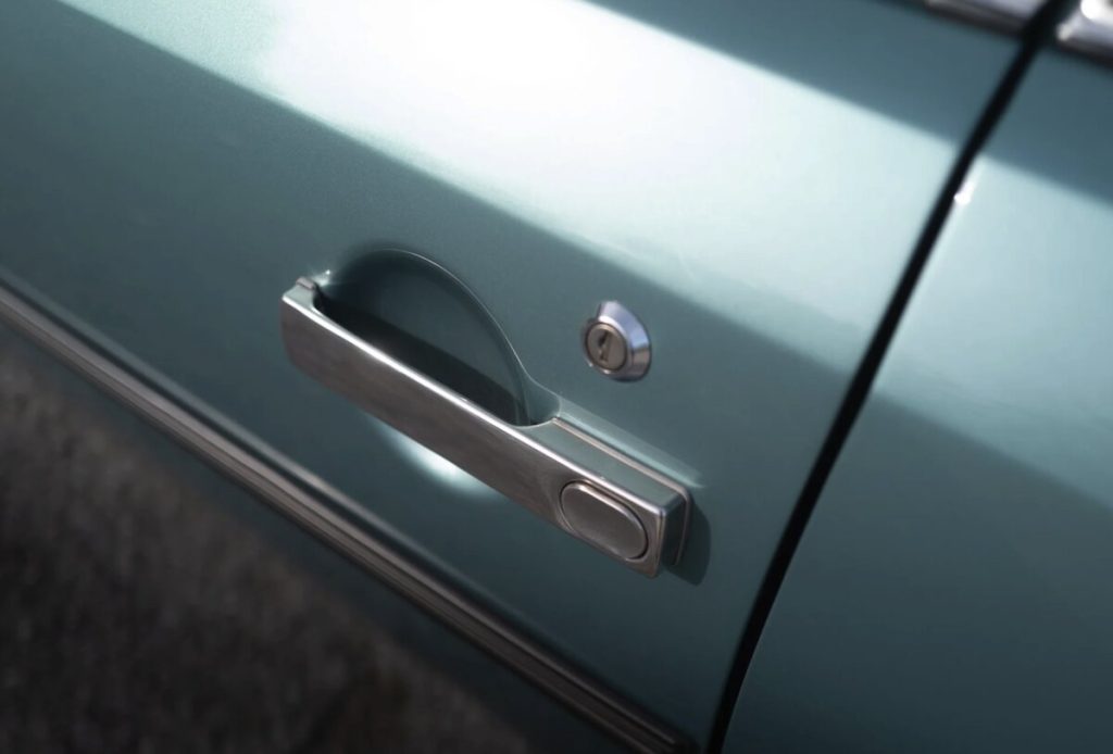 Macro detail of a chrome push-button door handle on the teal bodywork of a Citroën CX