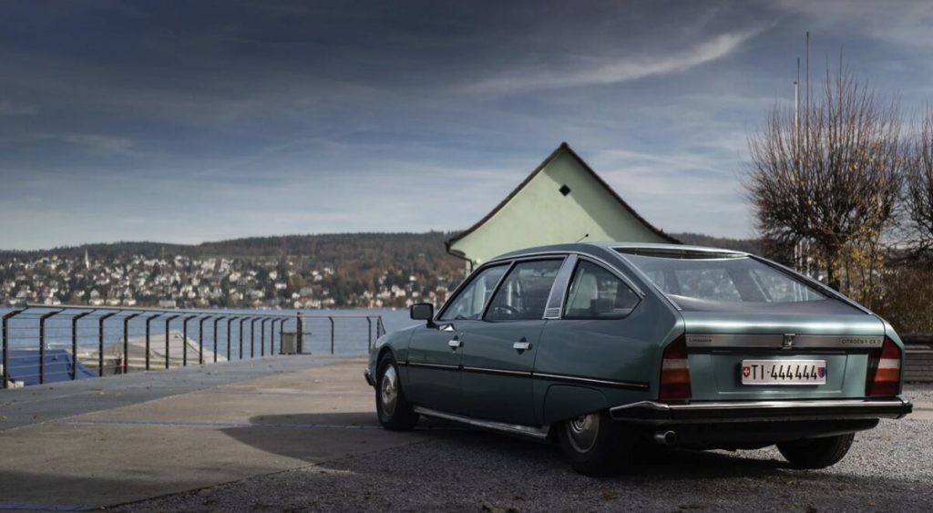 Rear three-quarter view of a teal green Citroën CX D Limousine parked on a lakeside promenade in Switzerland
