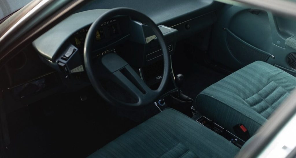 Citroën CX interior shot through the windscreen showing steering wheel, instrument cluster, and teal checked fabric seats