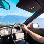 Driver's-eye view from inside a classic Porsche 944, with Lake Geneva and the Swiss Alps visible through the windscreen