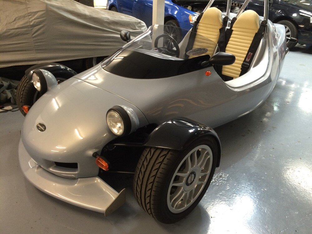 Silver Grinnall Scorpion III BMW-powered three-wheel sports car photographed indoors in a dealership