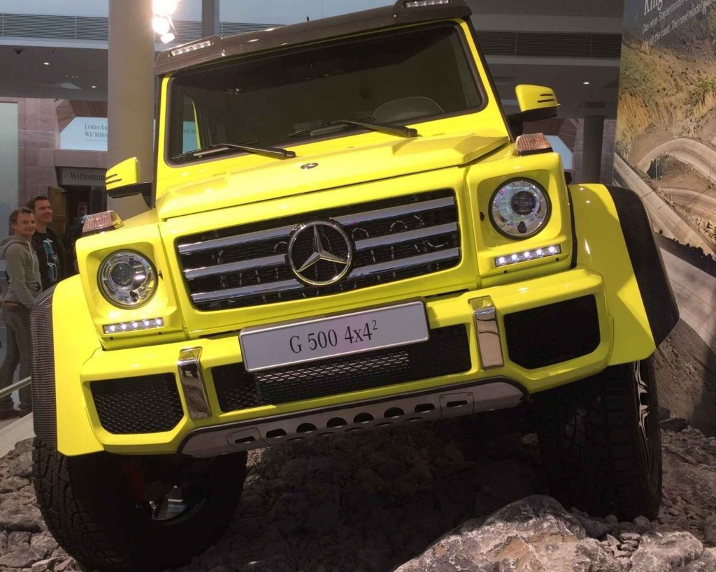 A neon yellow Mercedes-Benz G500 4x4² on display at a motor show, its towering portal axles and aggressive stance