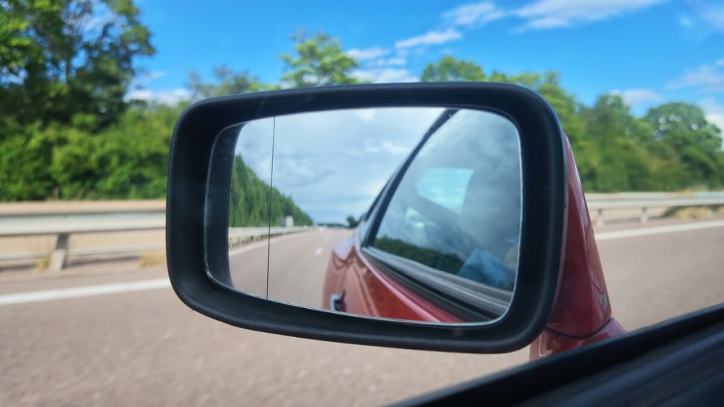 View from inside a red Porsche 944 of the driver's side wing mirror reflecting an empty French autoroute