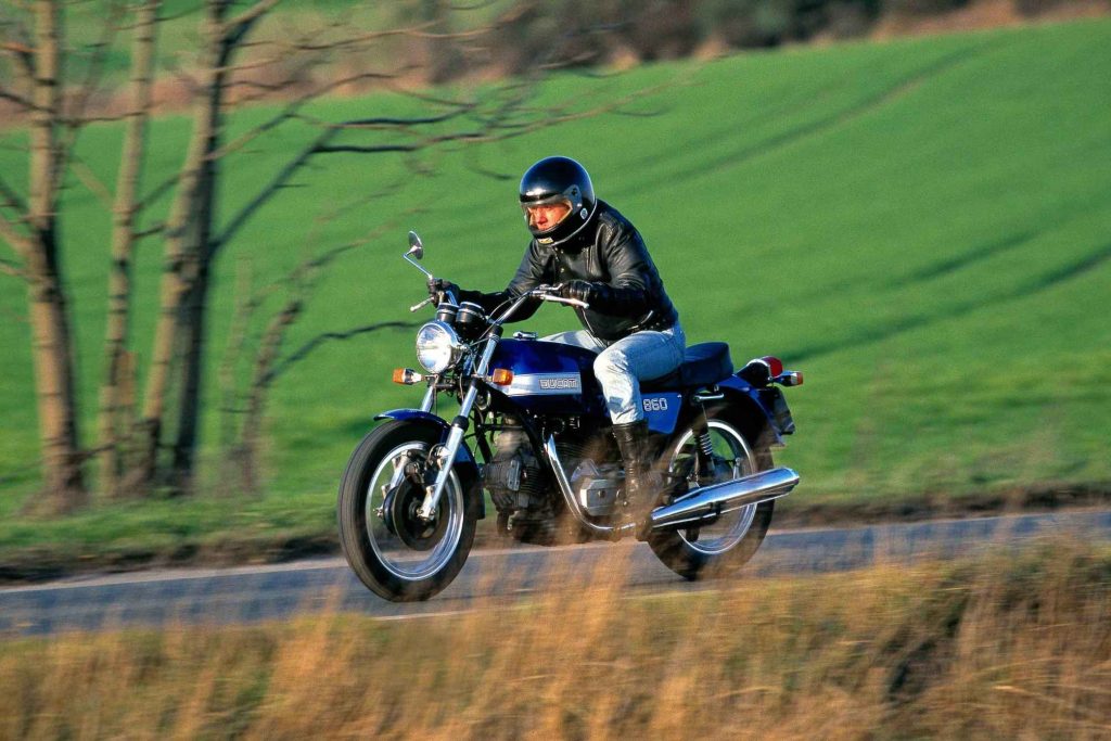 Rider in black helmet and leather jacket riding a classic Ducati 860 on a country road