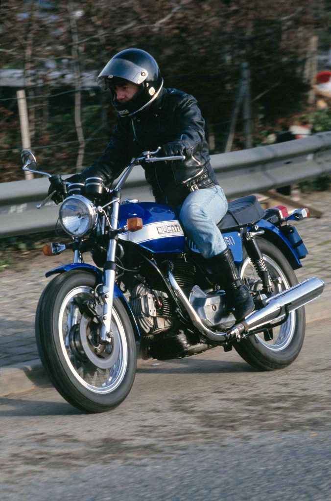 Rider cornering on a vintage blue Ducati 860 motorcycle on a cobbled road