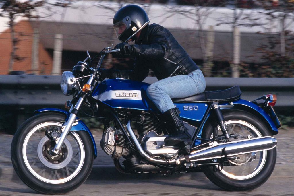 Rider cornering on a vintage blue Ducati 860 motorcycle on a cobbled road