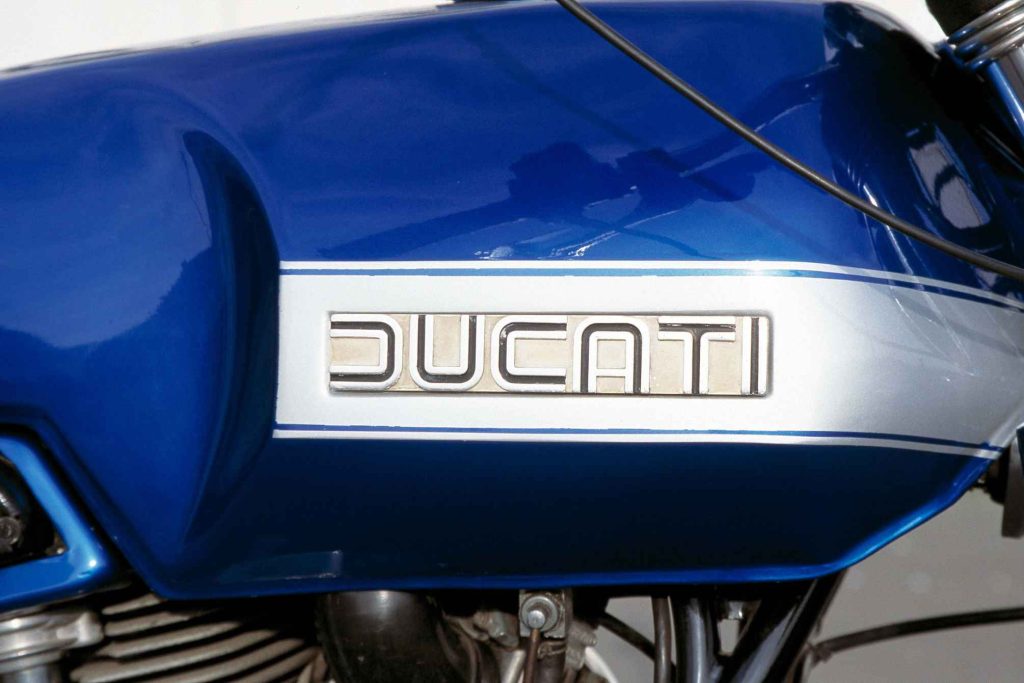 Close-up of a Ducati 860 L-twin engine with aluminum cases and blue and silver fuel tank
