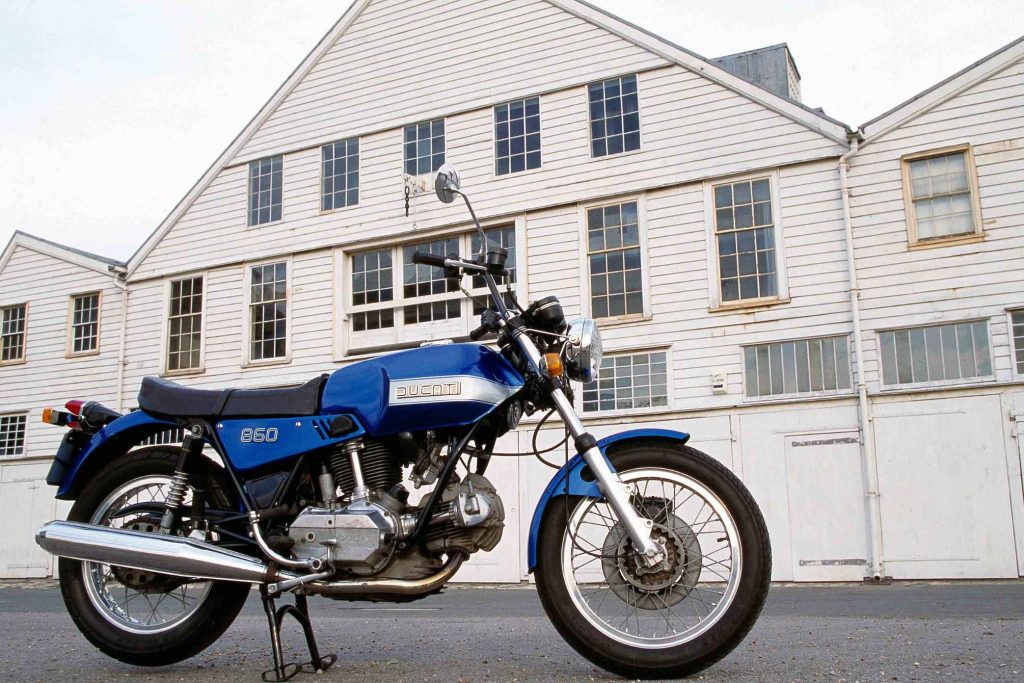 Blue and silver Ducati 860 vintage motorcycle parked in front of a white building