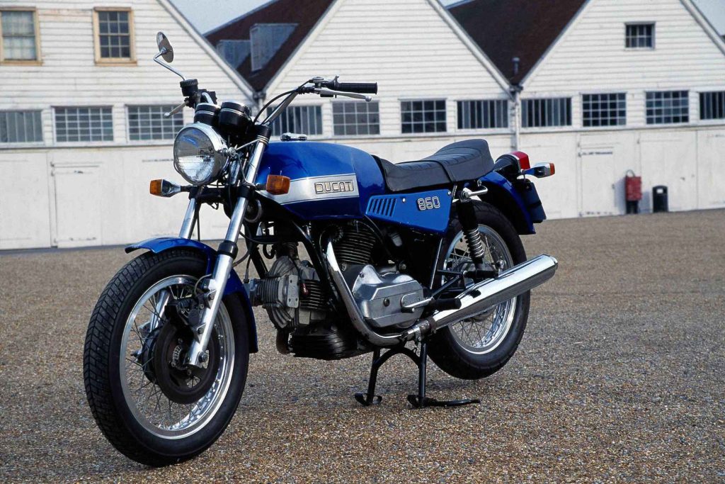 Blue and silver Ducati 860 vintage motorcycle parked in front of a white building