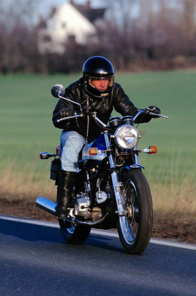 Rider in black helmet and leather jacket riding a classic Ducati 860 on a country road
