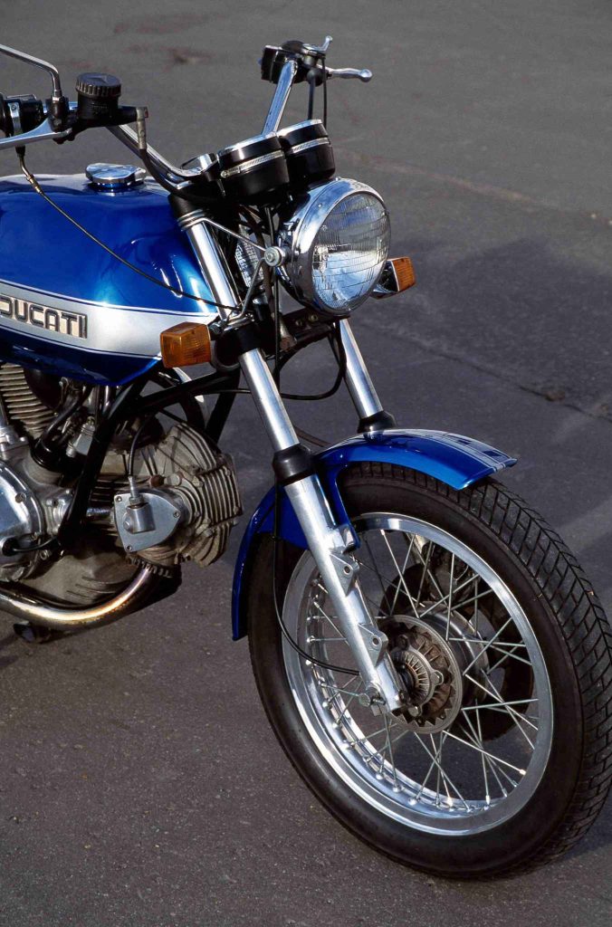 Front-right view of a classic blue Ducati 860 showing headlight, gauges and chrome forks