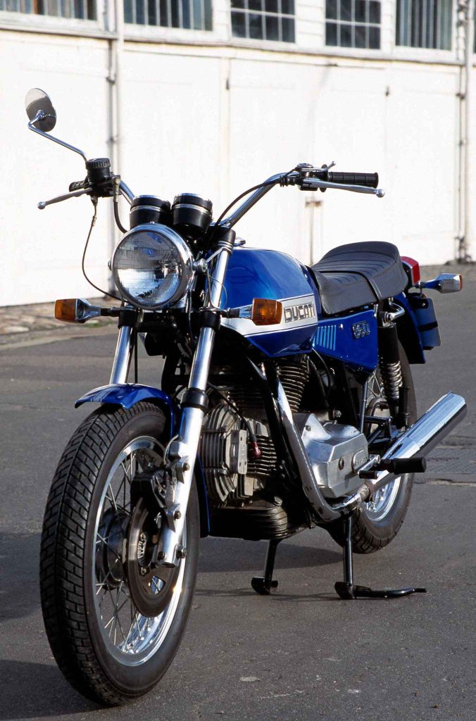 Blue and silver Ducati 860 vintage motorcycle parked in front of a white building