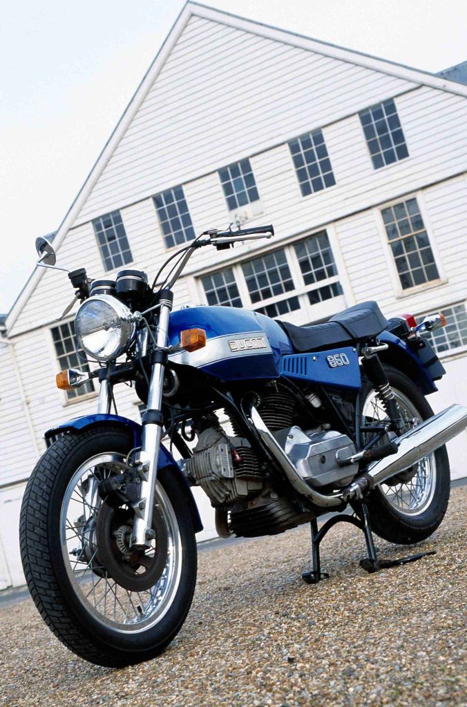 Blue and silver Ducati 860 vintage motorcycle parked in front of a white building