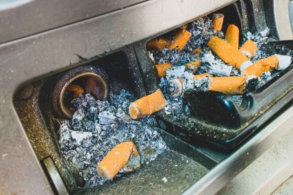 Overflowing car ashtray filled with cigarette butts and ash