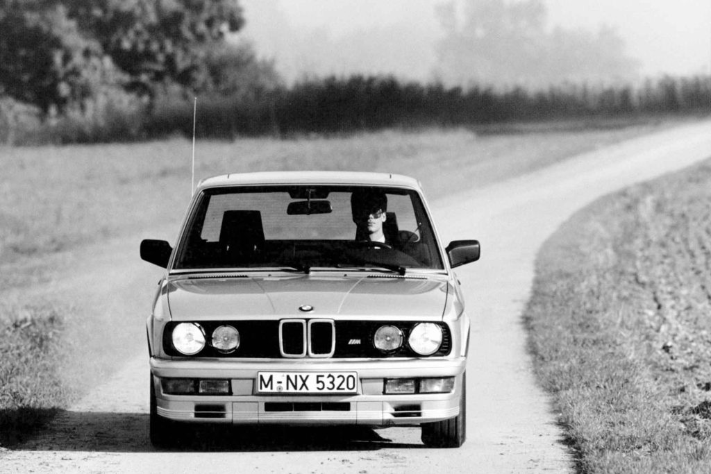 Black and white period press photograph of a silver BMW M535i E28 five-series saloon driven straight toward the camera