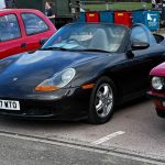 Front three-quarter view of a black Porsche Boxster 986 roadster with the roof down parked at an outdoor classic car show