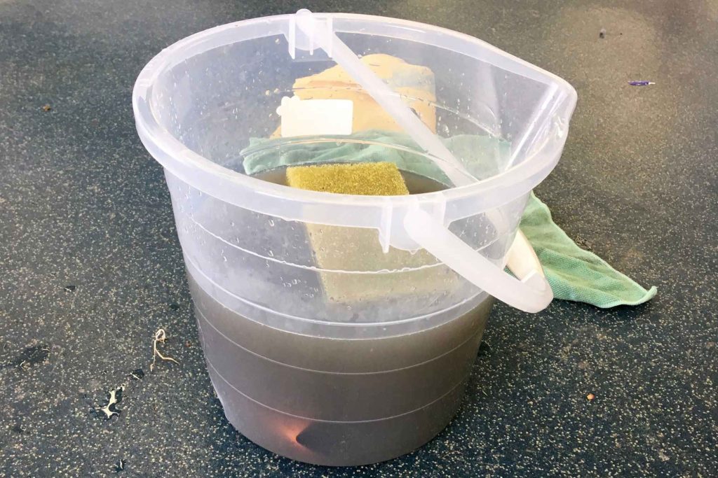 Plastic bucket of dirty wash water with sponge and cloth used for cleaning a car interior