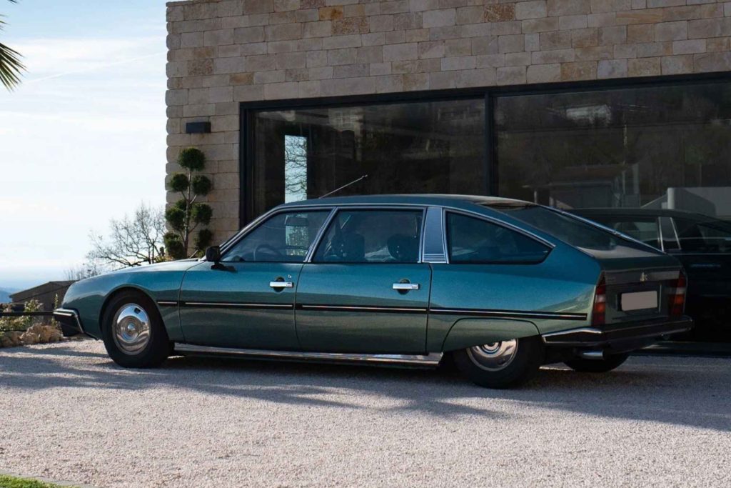Left-side profile of a dark green Citroën CX diesel parked on a gravel driveway outside a modern stone-clad villa