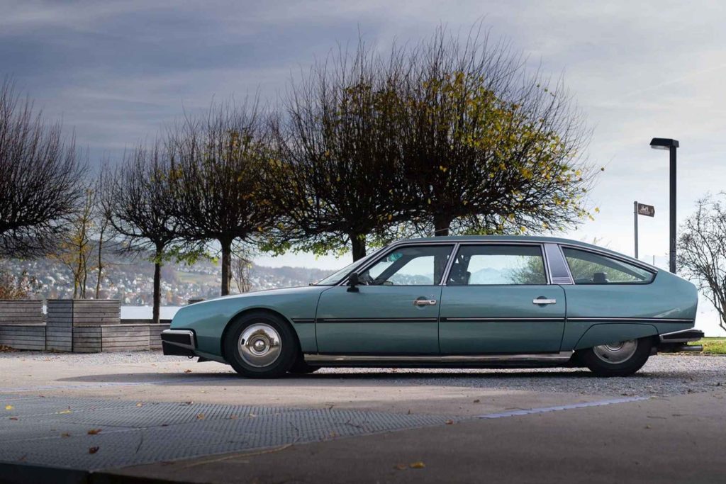 Full left-side profile of a teal green Citroën CX D parked on a lakeside promenade