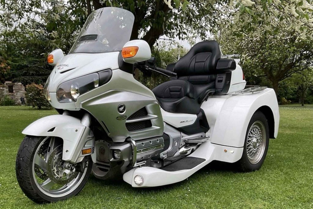 White Honda Gold Wing 1800 trike conversion photographed on a lawn in front of flowering trees
