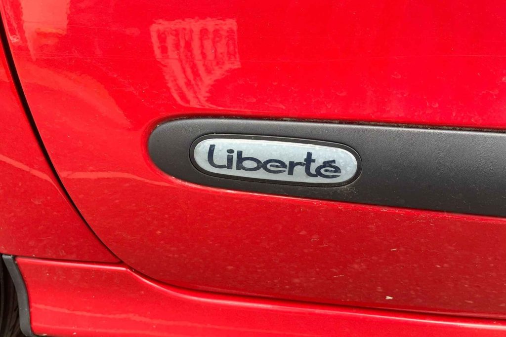 Close-up of a "Liberté" special edition badge set into a black side rubbing strip on a red Renault Twingo