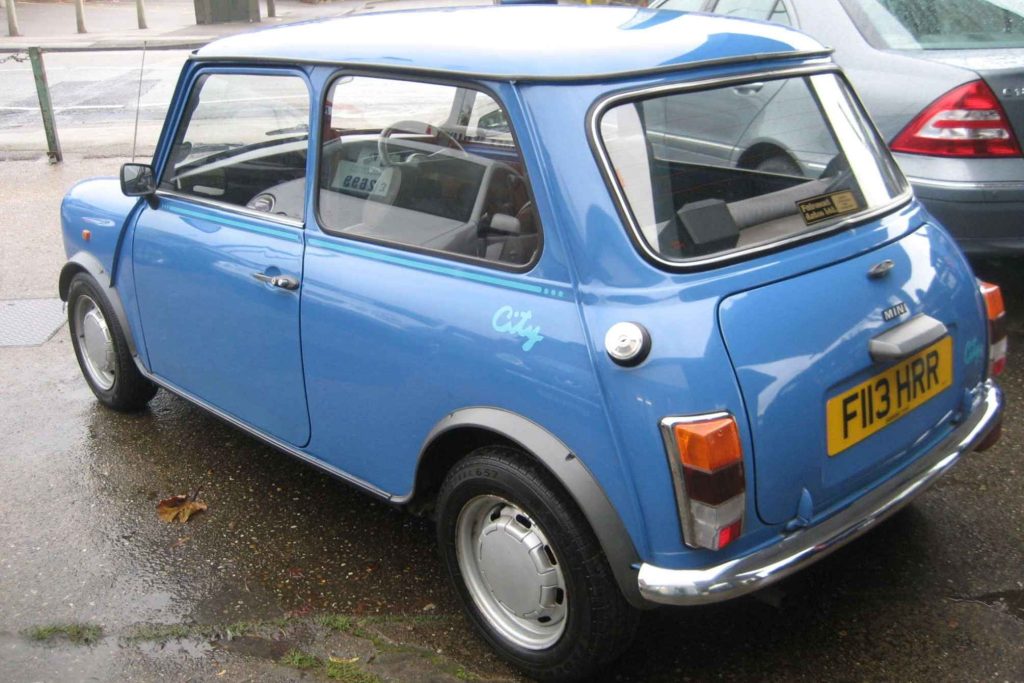 Rear three-quarter view of a blue Austin Mini City special edition parked on a wet street.