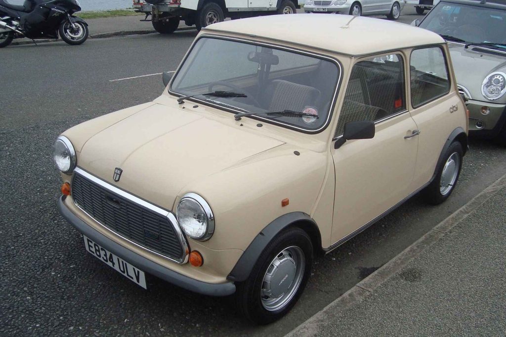 Front three-quarter view of a cream Austin Mini parked in a car park alongside a modern BMW Mini.