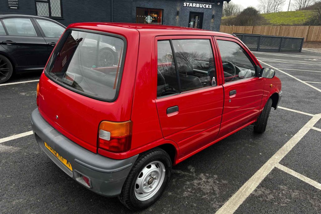 Rear three-quarter view of a red Daewoo Tico five-door city car parked in a car park outside a Starbucks