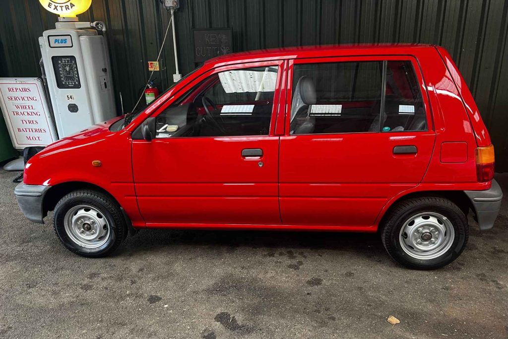 Left-side profile of a red Daewoo Tico five-door city car parked outside a vintage petrol station forecourt