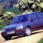 Peugeot 309 GTI in dark blue with red side stripe, front three-quarter shot on country lane in spring