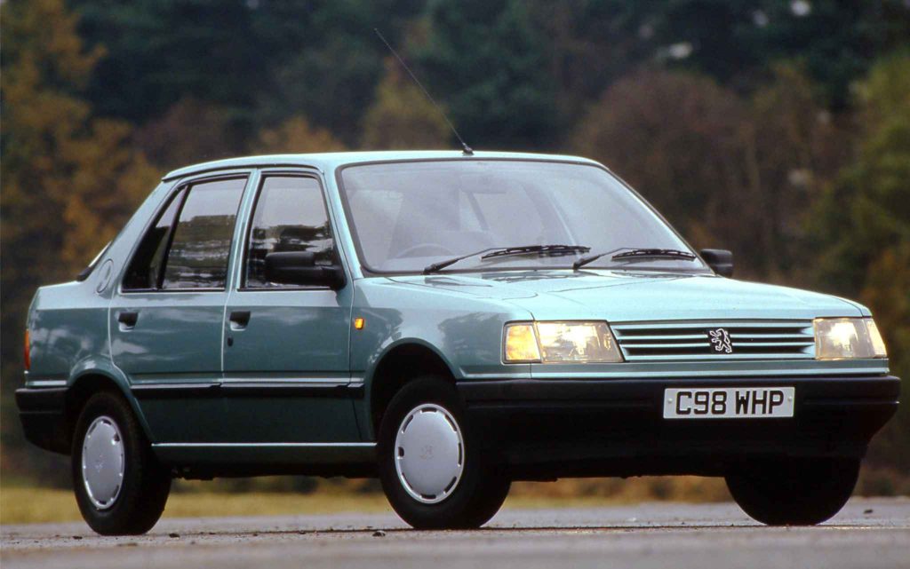 Peugeot 309 five-door hatchback in pale blue, UK press photo with autumn trees in background